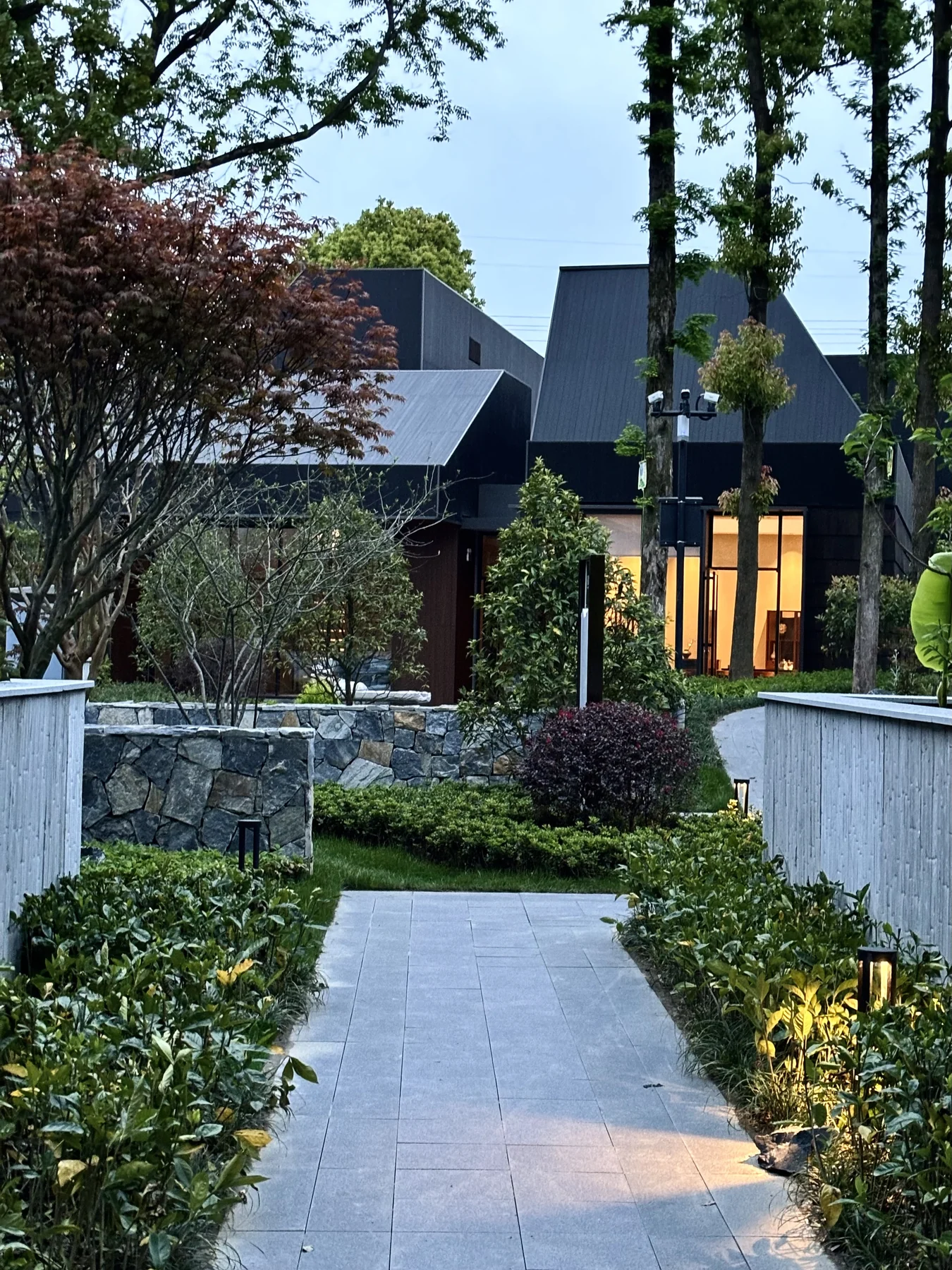 Built outdoor passage between guest accommodation buildings with planting and evening lighting
